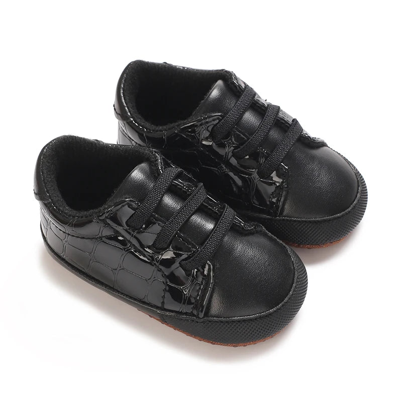 Pair of black baby shoes with crocodile texture on a white background
