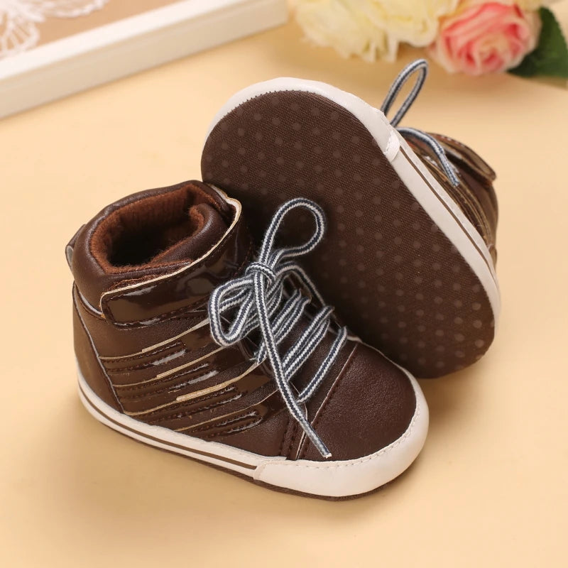 Pair of brown baby shoes with white laces on a beige surface.