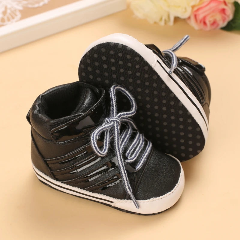 Black baby shoes with white soles on a beige surface