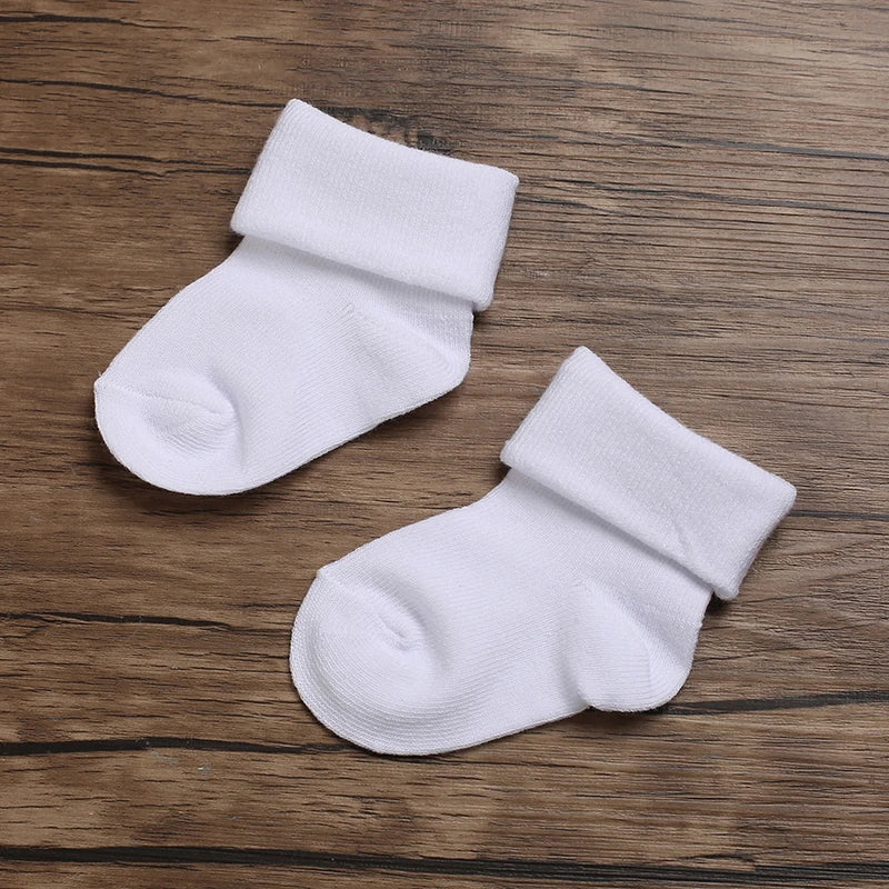Two white baby socks on a wooden surface