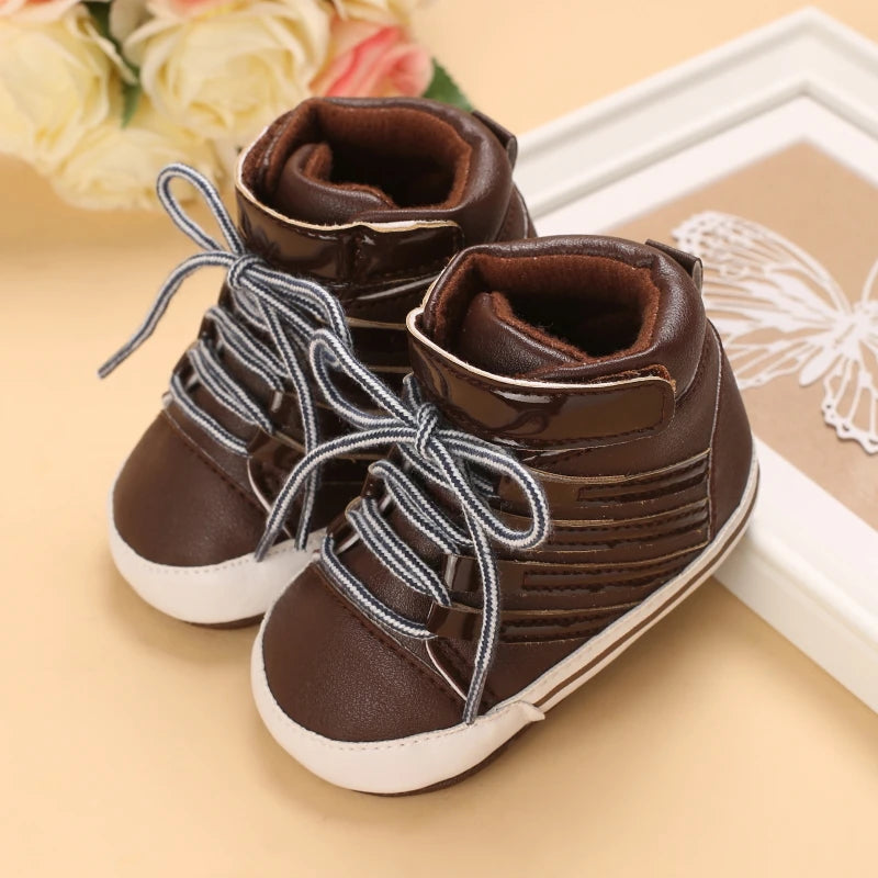 Pair of brown baby boots with white soles on a beige surface.