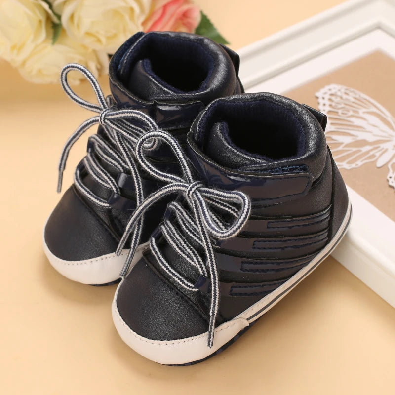 Pair of black baby boots with white soles on a beige surface.