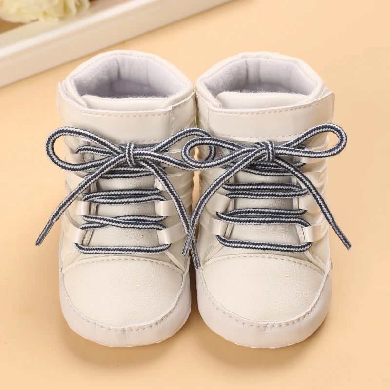 Pair of white baby shoes with blue laces on a beige background