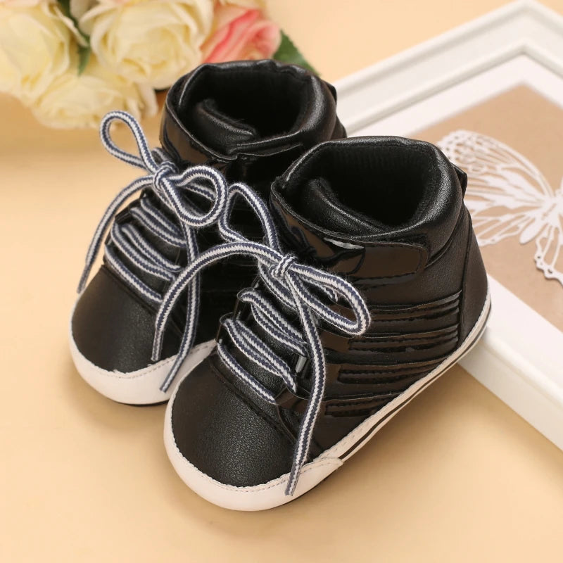 Black baby shoes with white soles on a beige surface