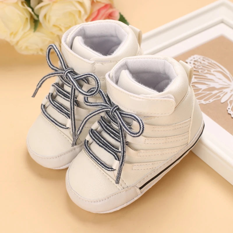 White baby shoes with blue laces on a beige surface with flowers in the background
