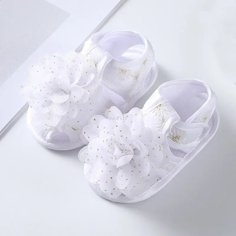 White baby sandals with floral details on a light gray background