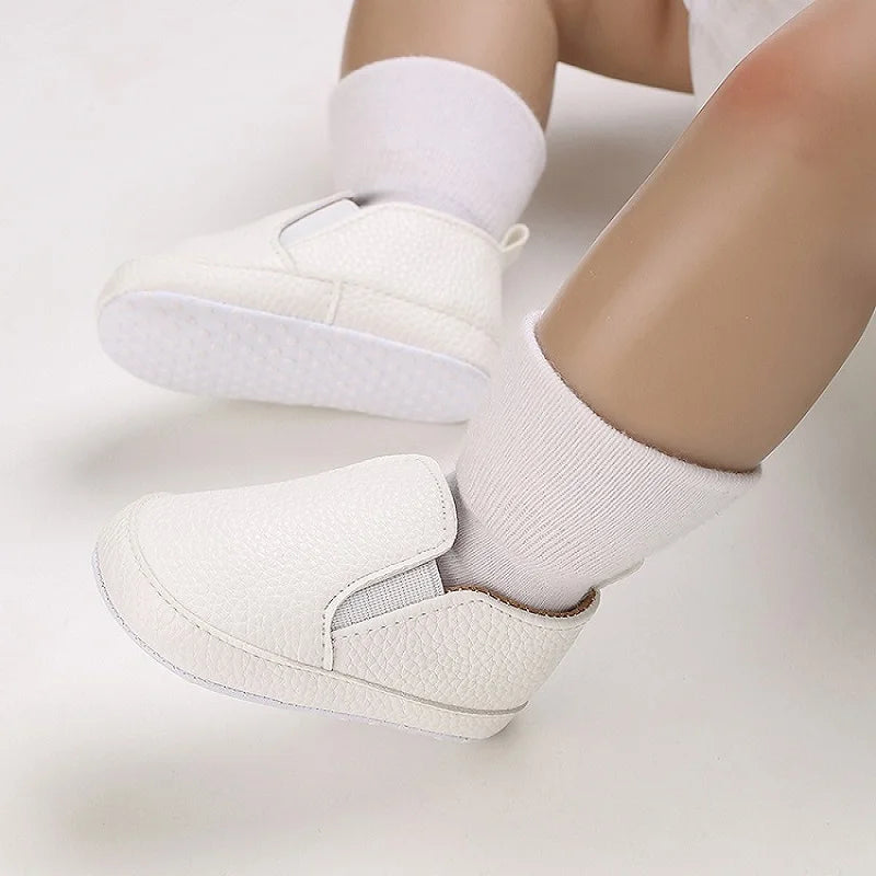 White baby shoes worn with white socks on a light background