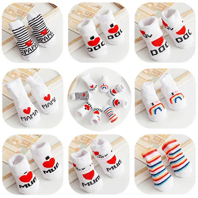 Set of baby socks with 'Mum', 'Dad', and rainbow designs on a wooden surface.