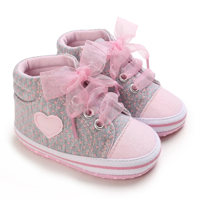 Pair of baby shoes with pink ribbons and hearts on a white background