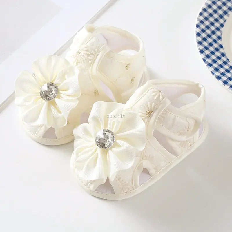 White baby sandals with floral designs and rhinestones on a white background