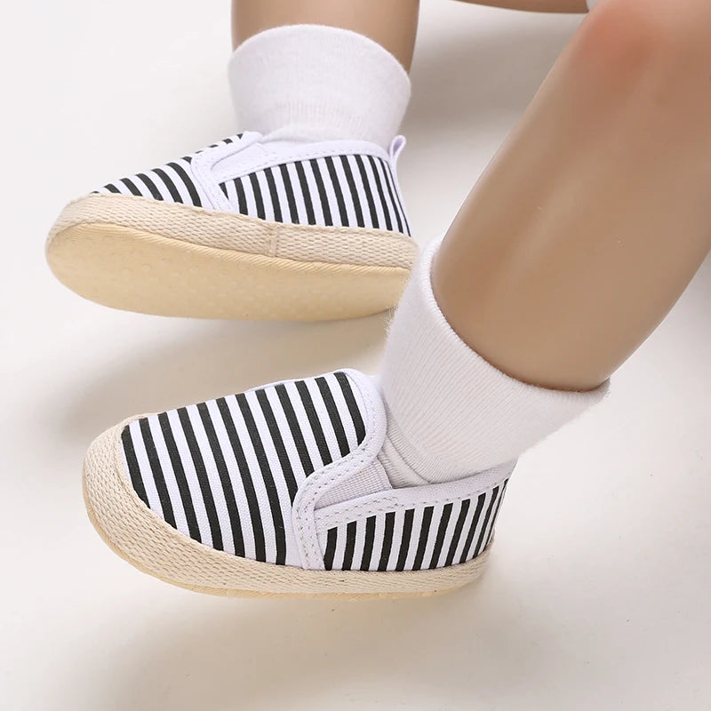 Black and white striped baby shoes with beige soles on a light background