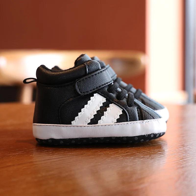 Black and white Adidas baby shoe on a wooden surface with a blurred background