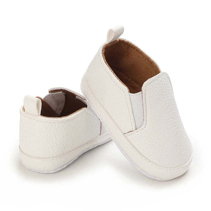 Pair of white baby shoes with brown soles on a white background