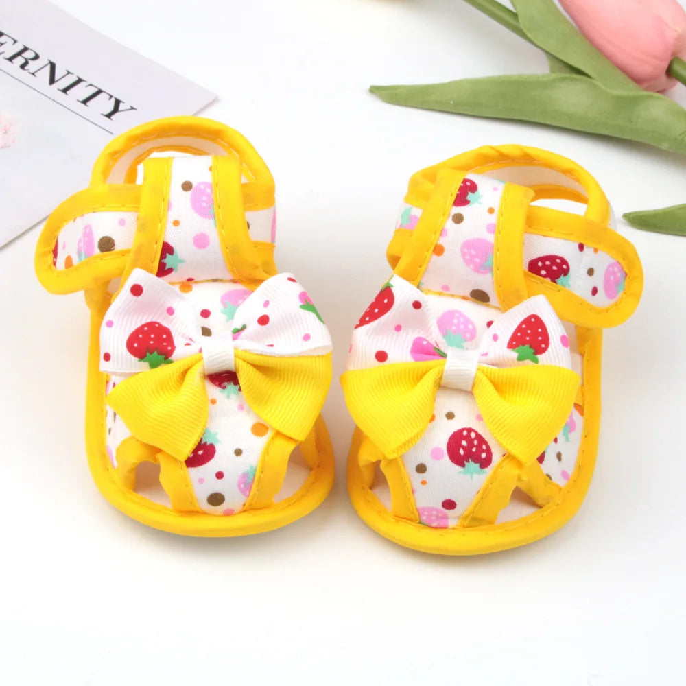 Pair of baby sandals with yellow bows and strawberry pattern on a white background