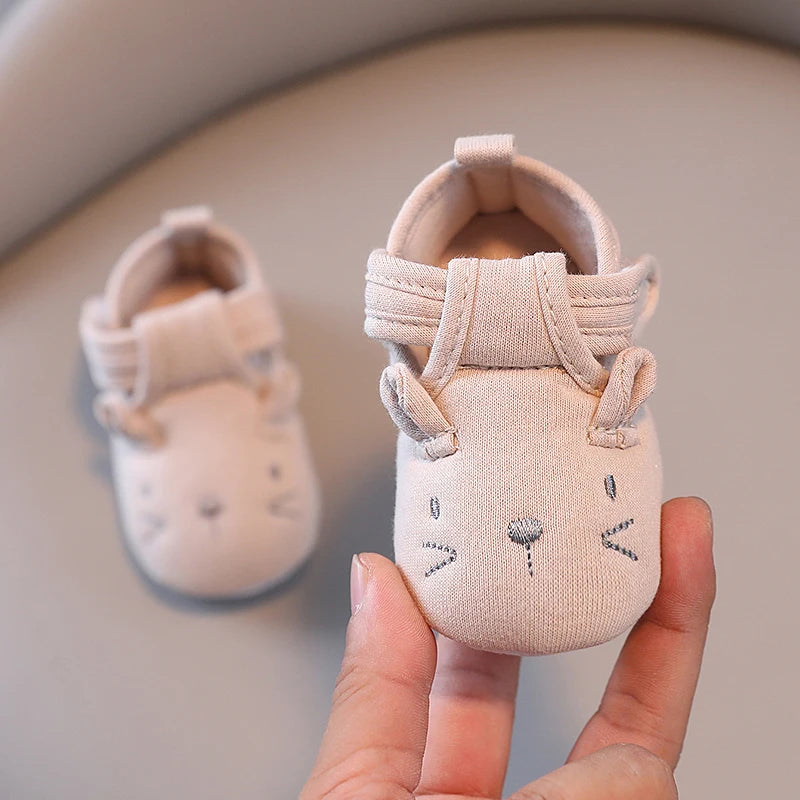 Baby shoes with unicorn design held by a hand on a neutral background