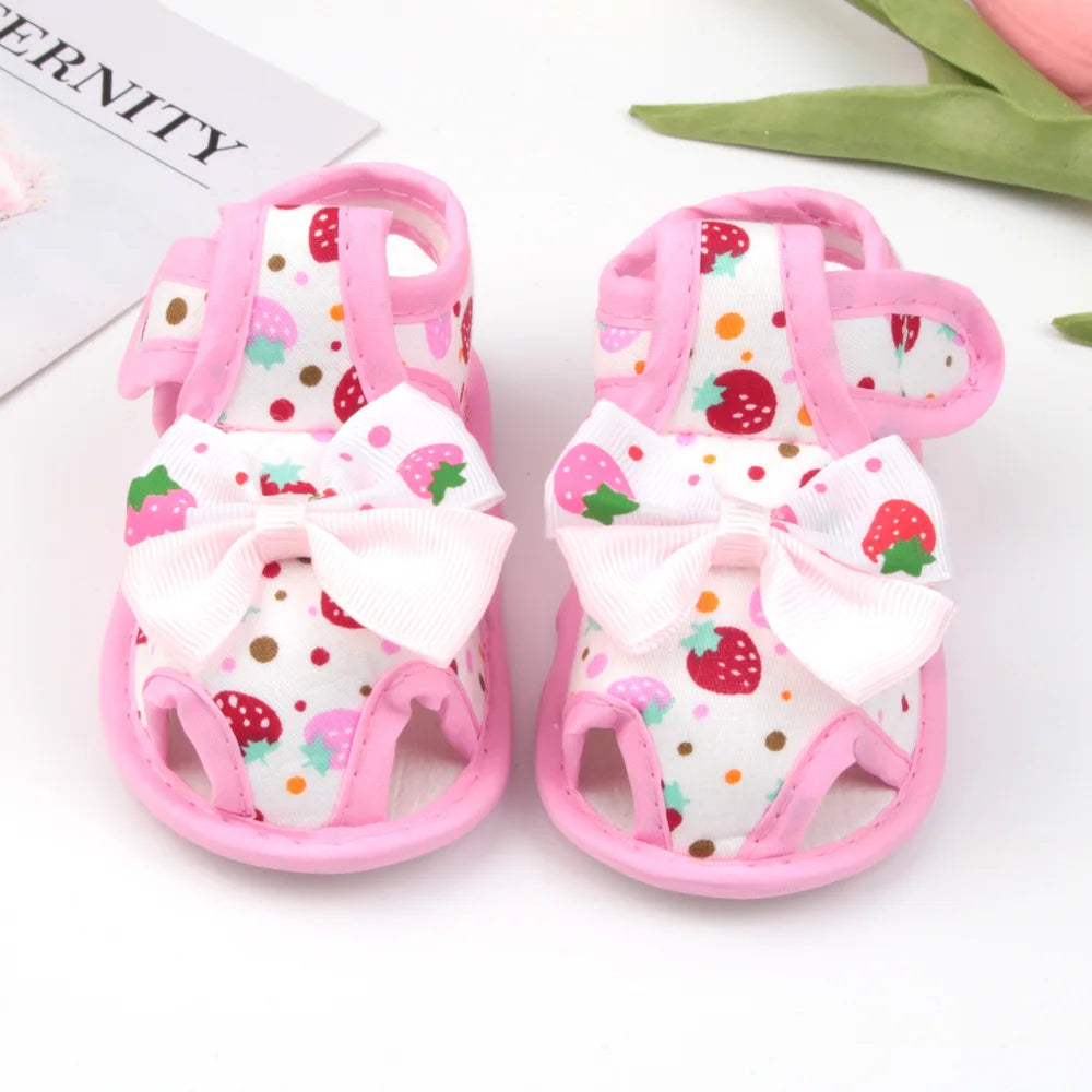 Pair of baby sandals with strawberry pattern and pink bows on a white background