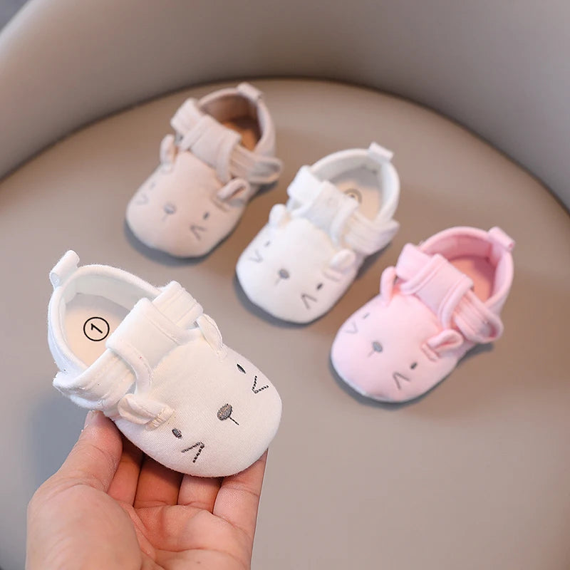 Set of baby shoes with cartoon faces, one held by a hand on a neutral background