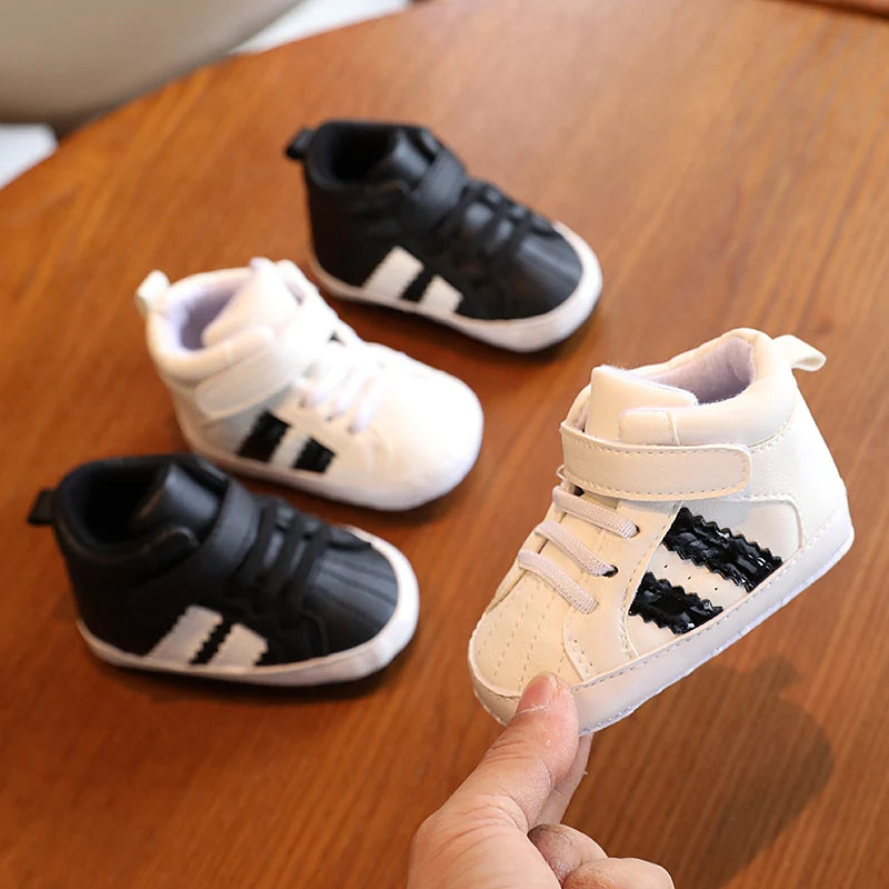 Pair of black and white baby shoes on a wooden surface with one shoe held by a hand.