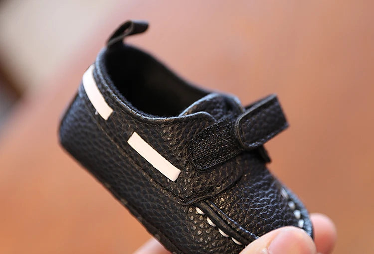 Black baby shoe with velcro straps held in a hand against a blurred background