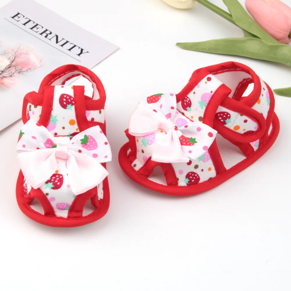 Red baby sandals with white bows and strawberry pattern on a white background