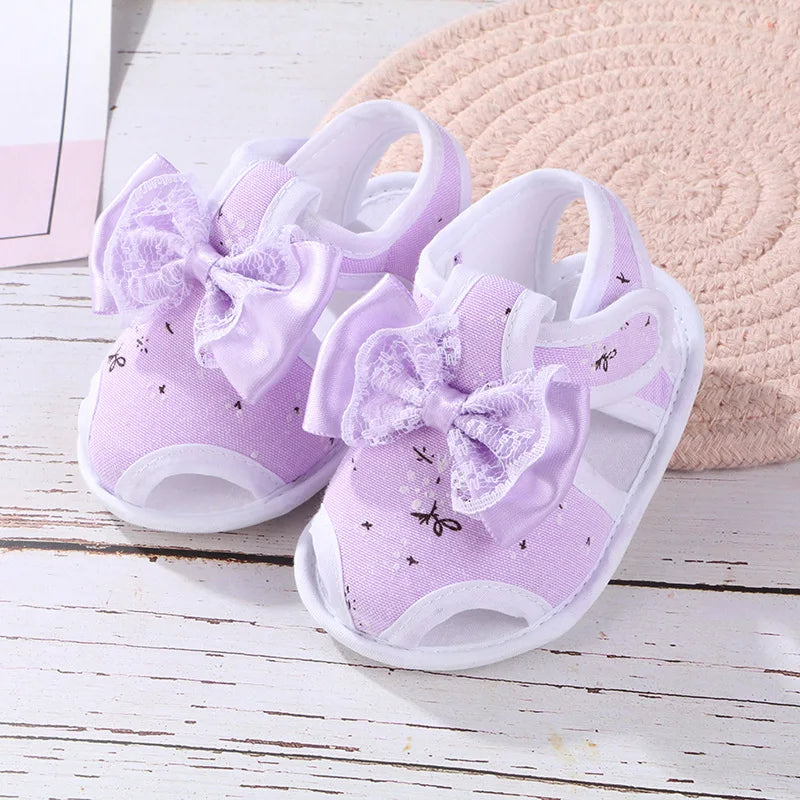 Pair of purple baby shoes with bows on a wooden surface