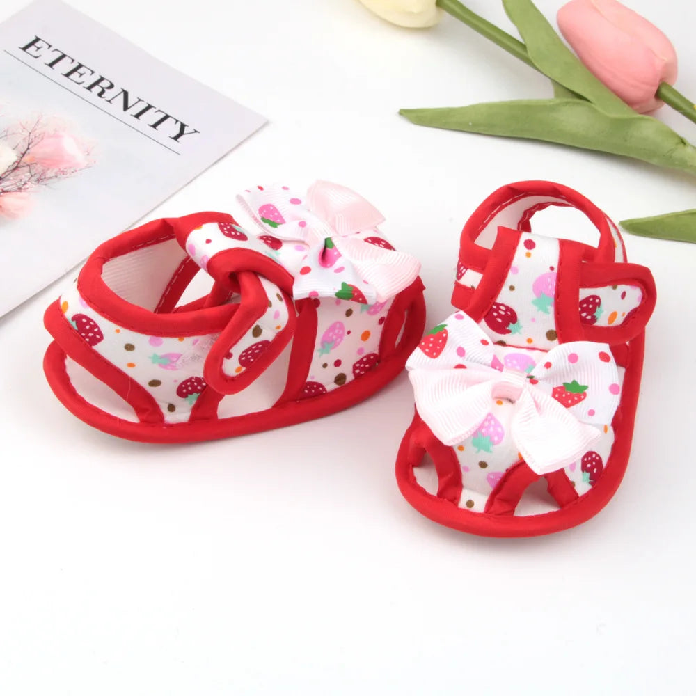 Red baby sandals with white bow and strawberry pattern on a white background