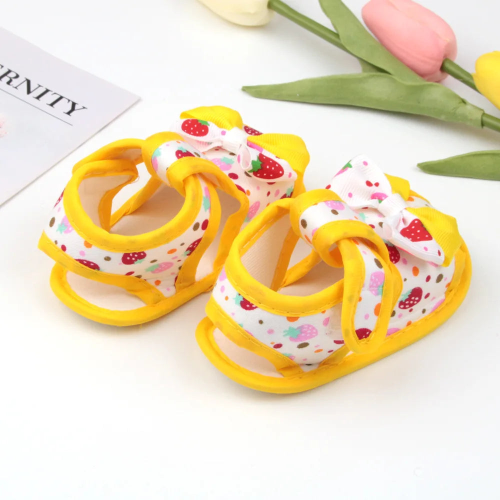 Pair of baby shoes with strawberry pattern on a white surface with tulips.