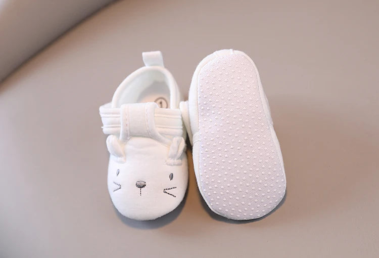 White baby shoes with cat face design on a beige surface