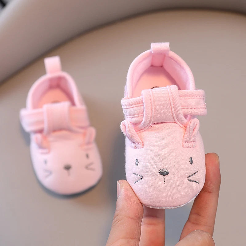 Pink baby shoes with bow design held by a hand against a neutral background