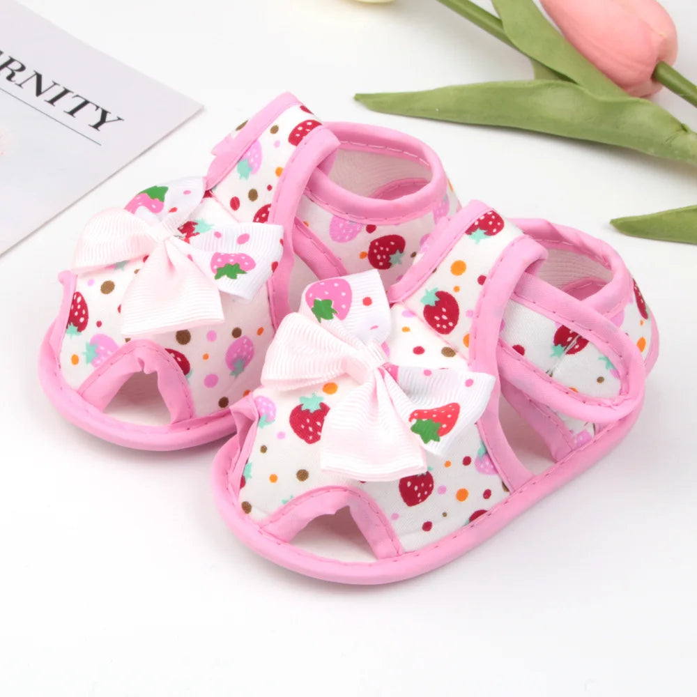 Pair of baby sandals with strawberry pattern and pink bows on a white background