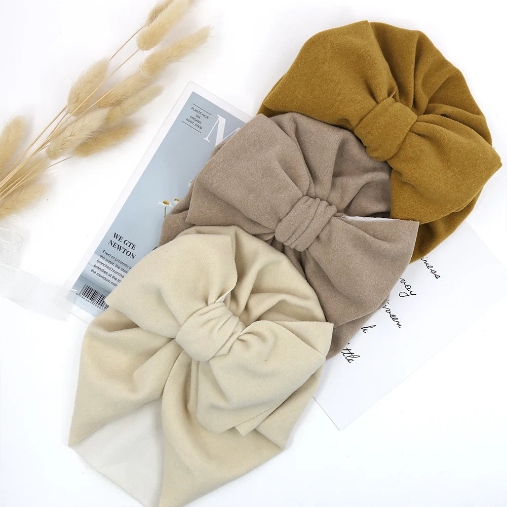 Three headbands in beige, brown, and mustard on a white surface with dried plants.
