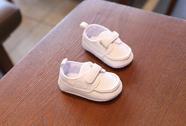 Pair of white baby shoes on a wooden surface