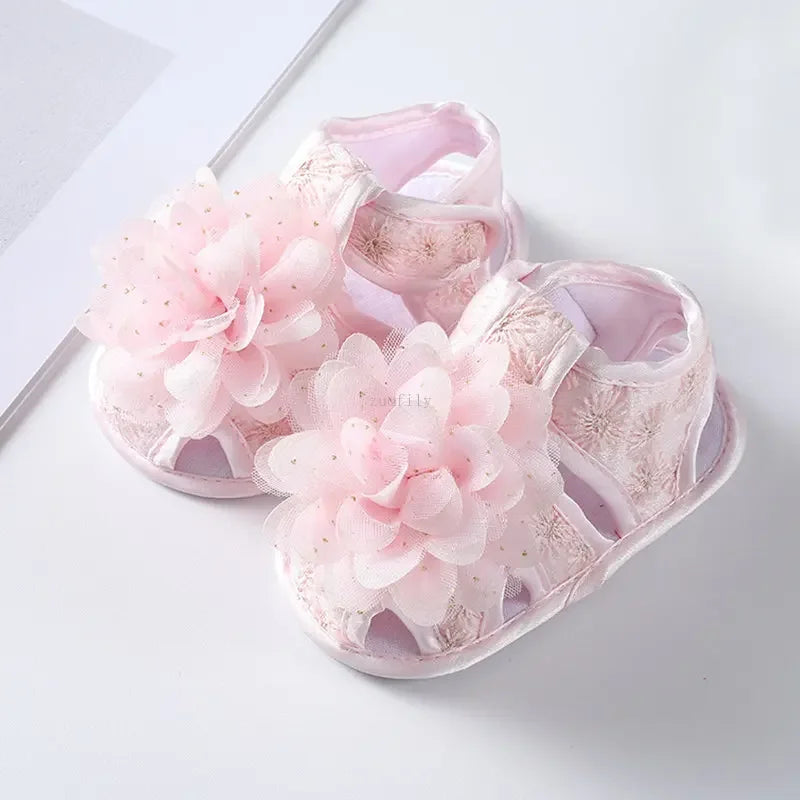 Pink baby sandals with floral details on a white background