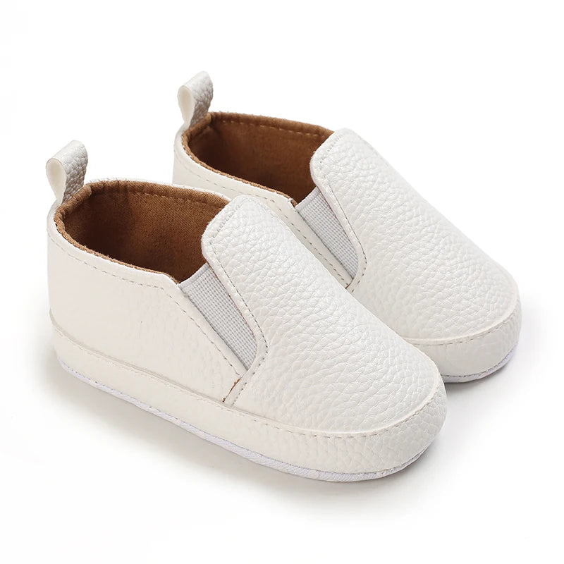 Pair of white baby shoes with brown soles on a white background