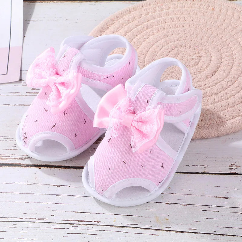 Pink baby sandals with bows on a wooden surface