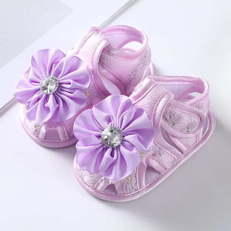 Purple baby sandals with floral designs and rhinestones on a white background