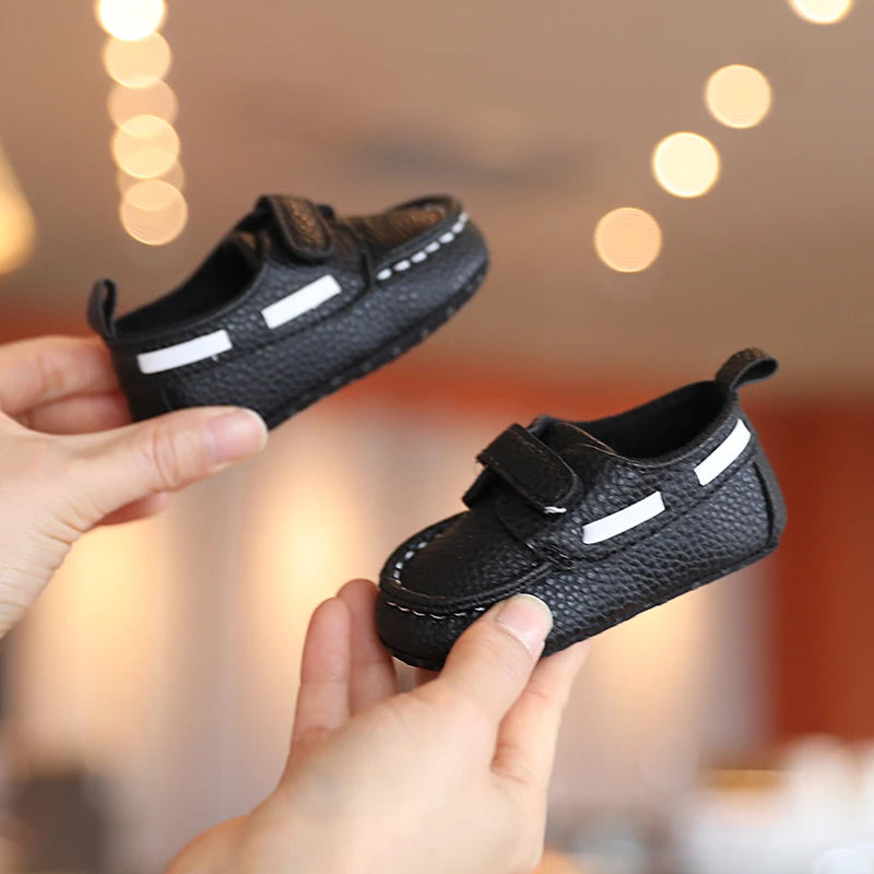 Black children's shoes with white stripes held by a person against a blurred background