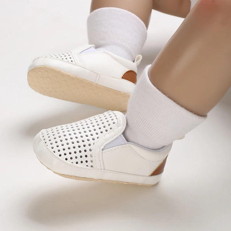 White baby shoes with beige soles worn by a child on a light background