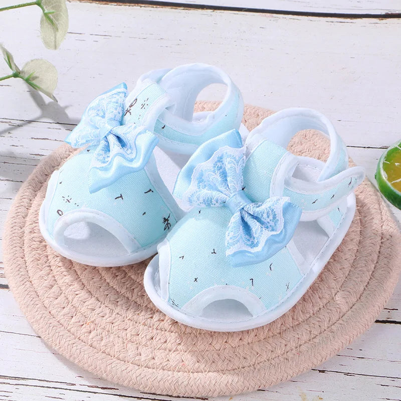 Pair of light blue baby sandals with bow details on a woven mat.