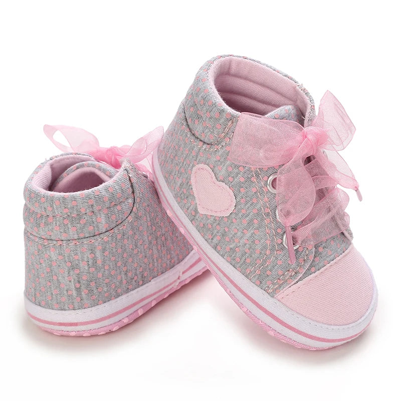 Pair of baby shoes with pink ribbons and heart design on a white background