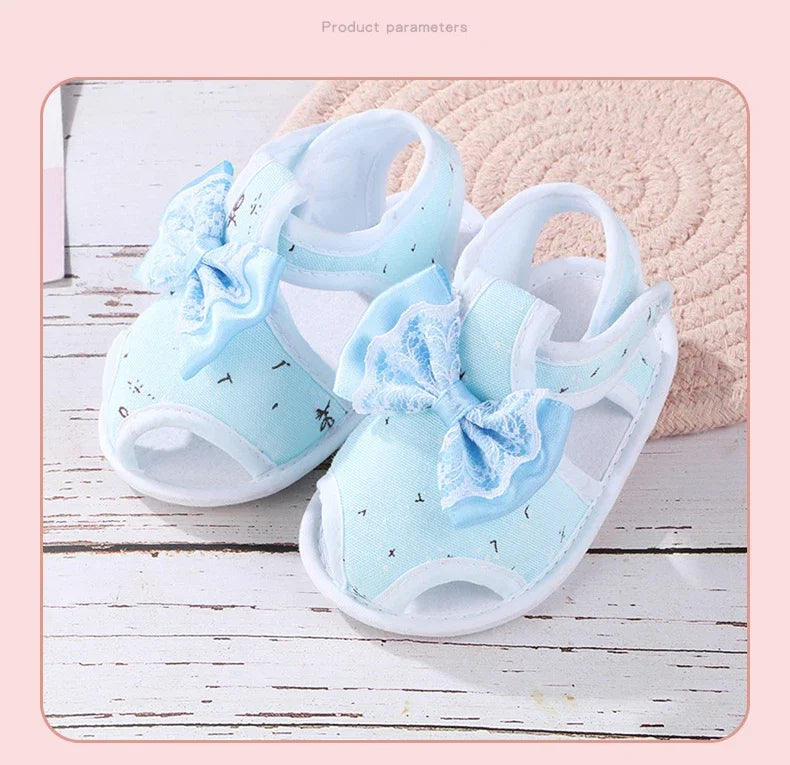 Pair of light blue baby sandals with bows on a wooden surface