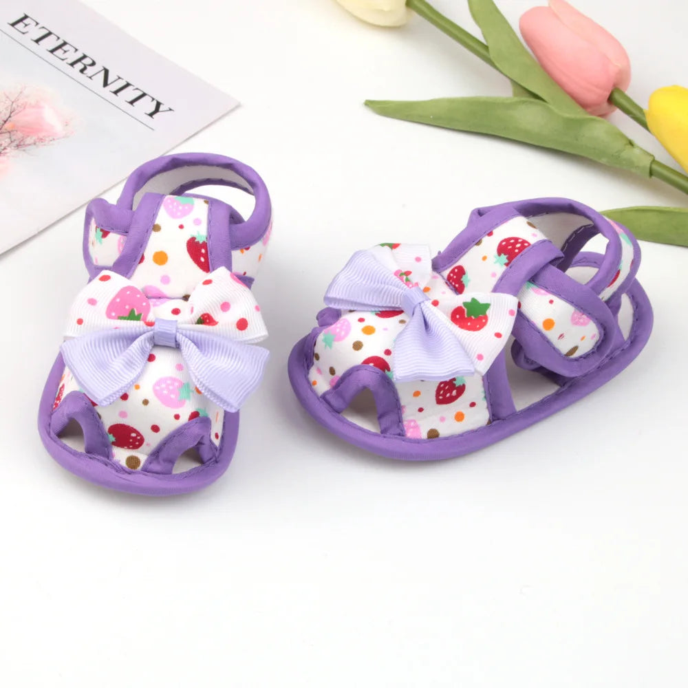 Pair of baby sandals with purple straps and colorful polka dot design on a white background.