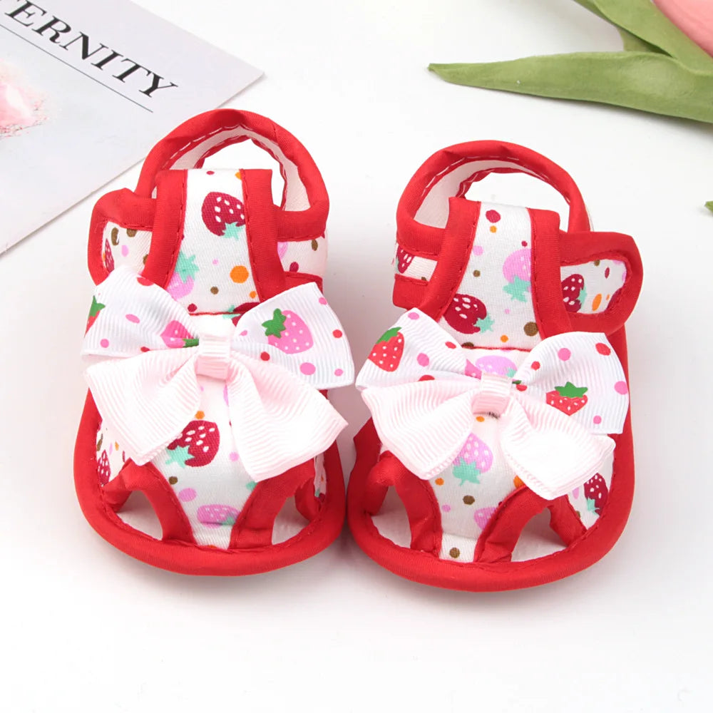 Red baby sandals with white bows and strawberry patterns on a white background