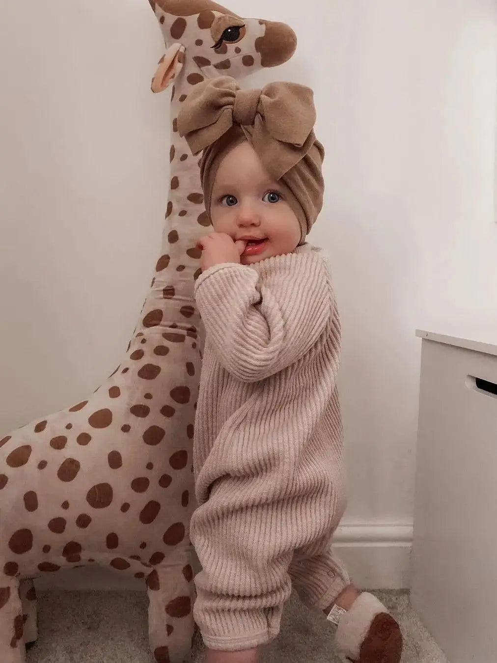 Baby in a beige outfit with a large stuffed giraffe toy