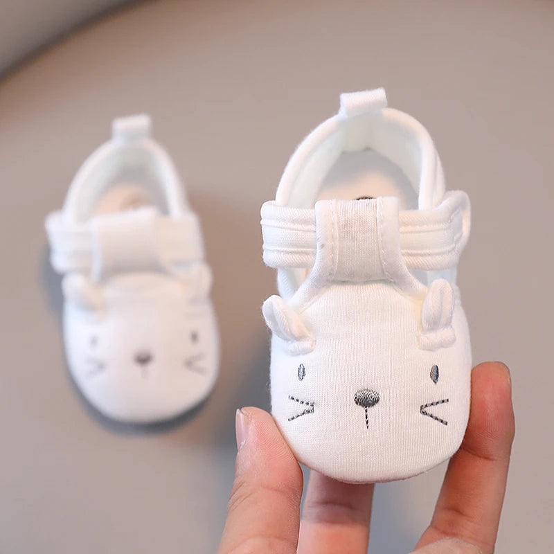 White baby shoes with animal face design held by a hand against a neutral background