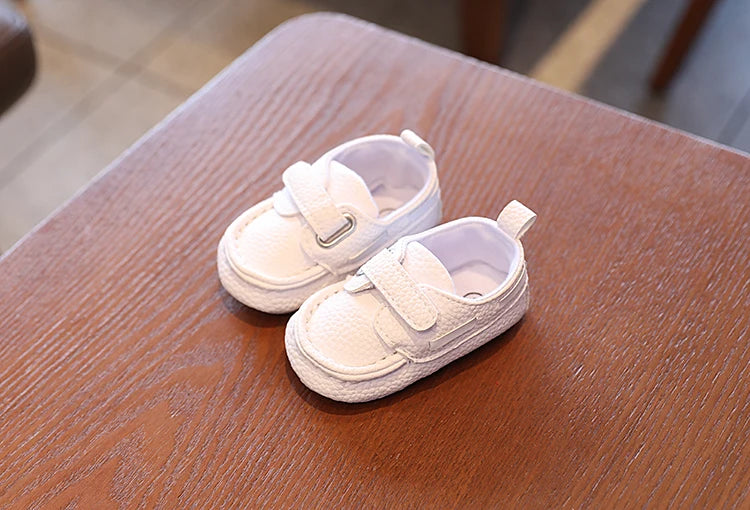 Pair of white baby shoes on a wooden surface