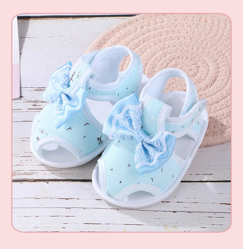 Pair of light blue baby sandals with bow details on a wooden surface.