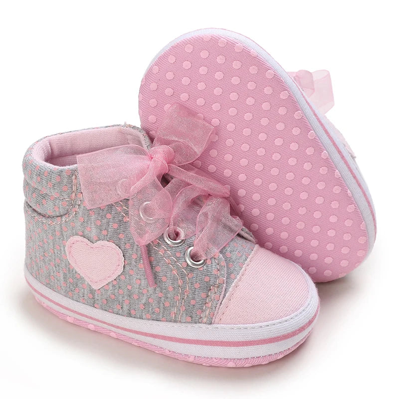 Pair of baby shoes with pink polka dots and heart design on a white background