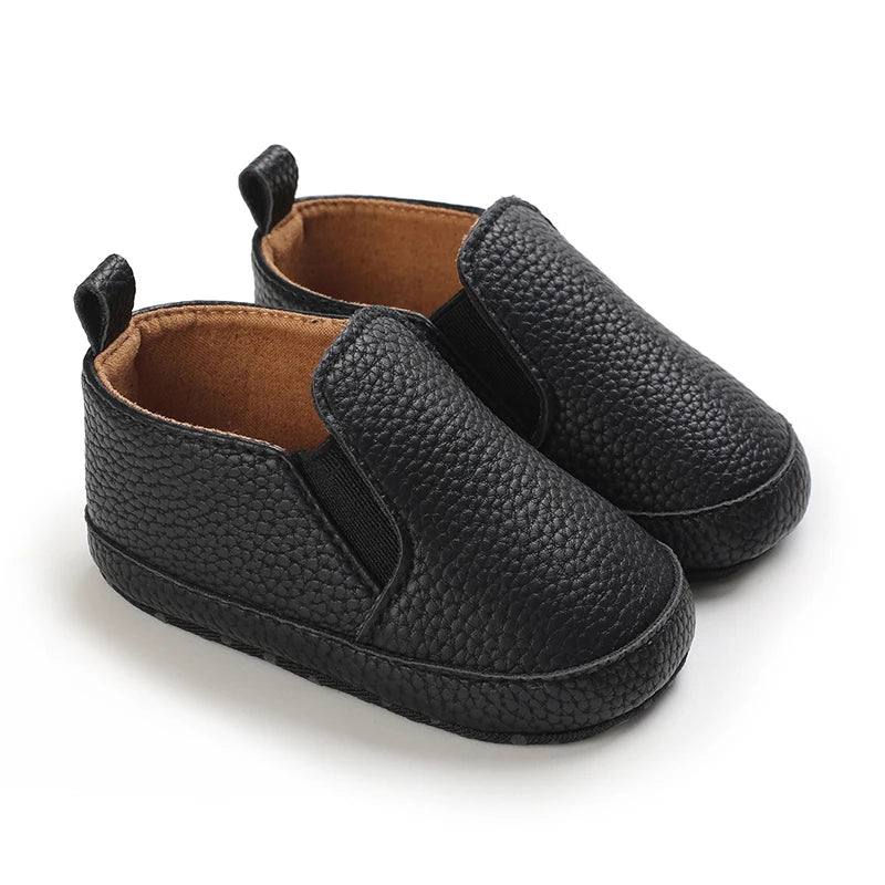 Pair of black baby shoes with brown soles on a white background
