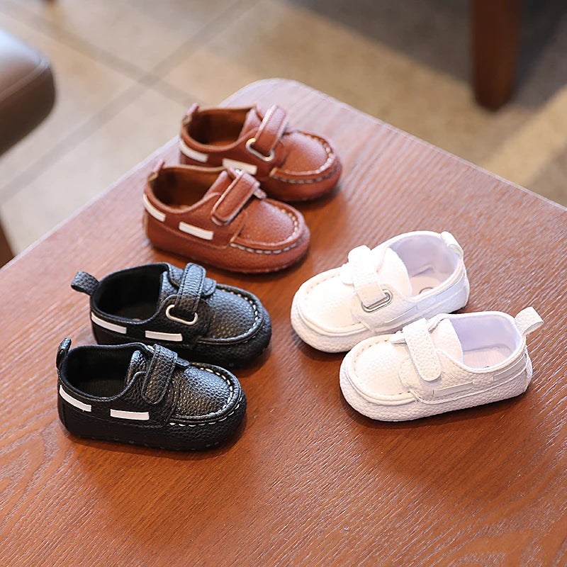 Set of children's shoes including brown, black, and white pairs on a wooden surface.